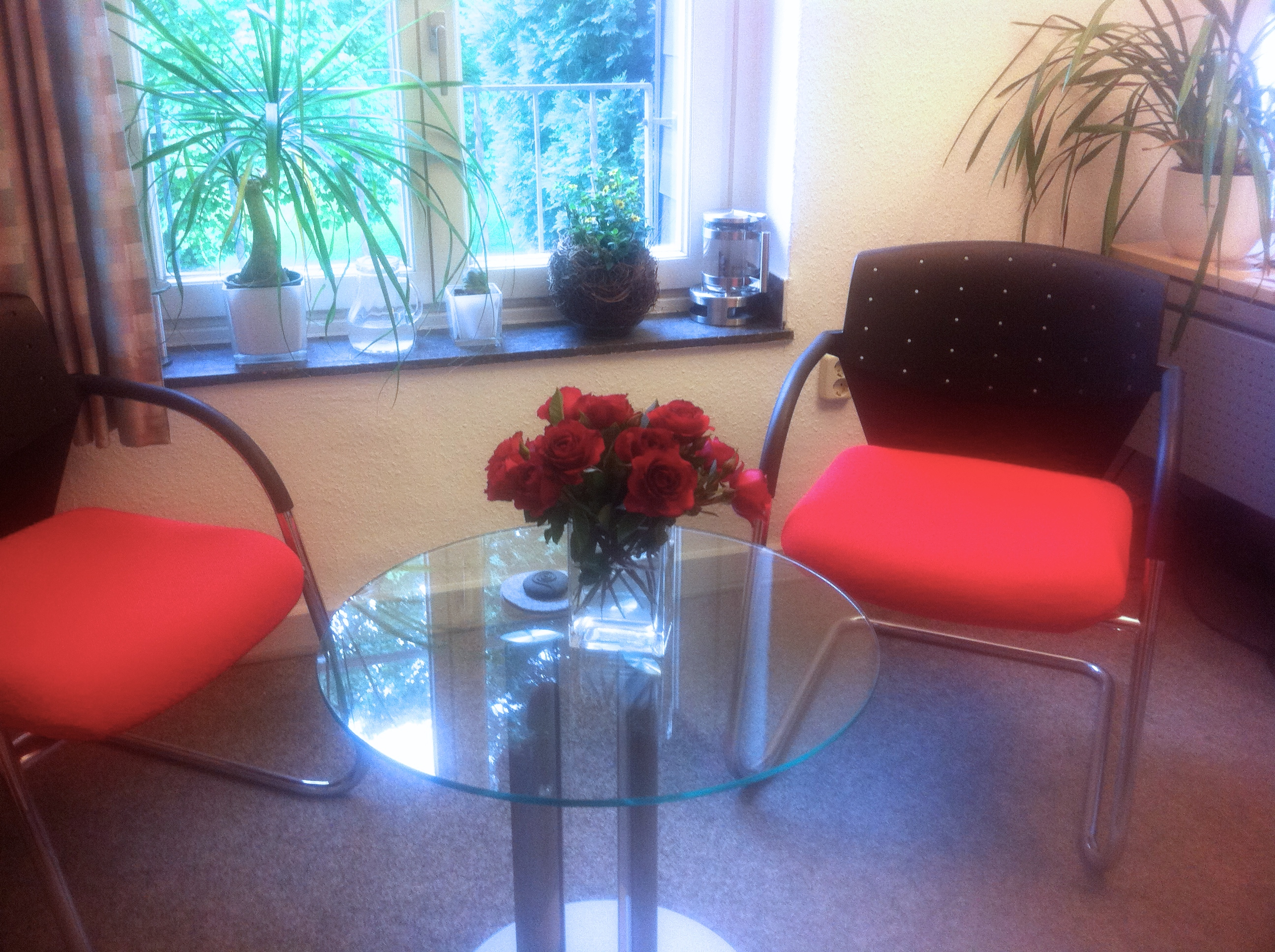 Sitzgruppe mit Glastisch und Blumenschmuck am Fenster