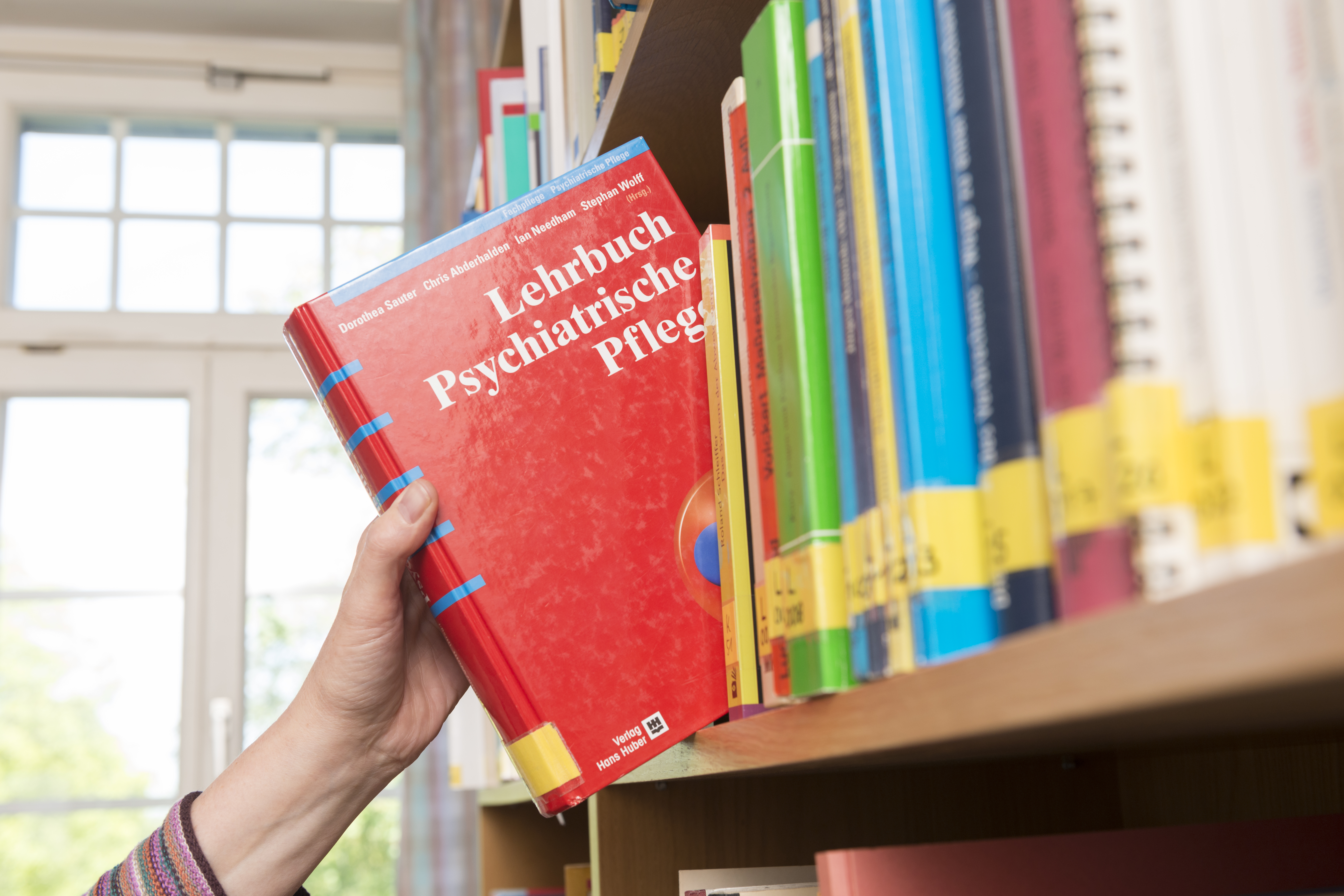 Hand greift nach einem Fachbuch im Bücherregal